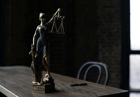Lady Justice figurine on wooden table in dimly lit room symbolizes law and fairness.